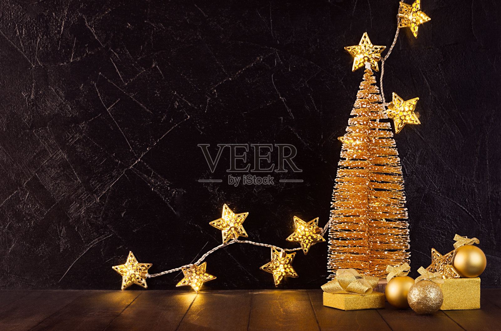豪华的家庭装饰新年派对-金色的圣诞树，发光的灯与星星，球，礼盒，丝带在黑暗的室内木制桌子上，拷贝空间。照片摄影图片