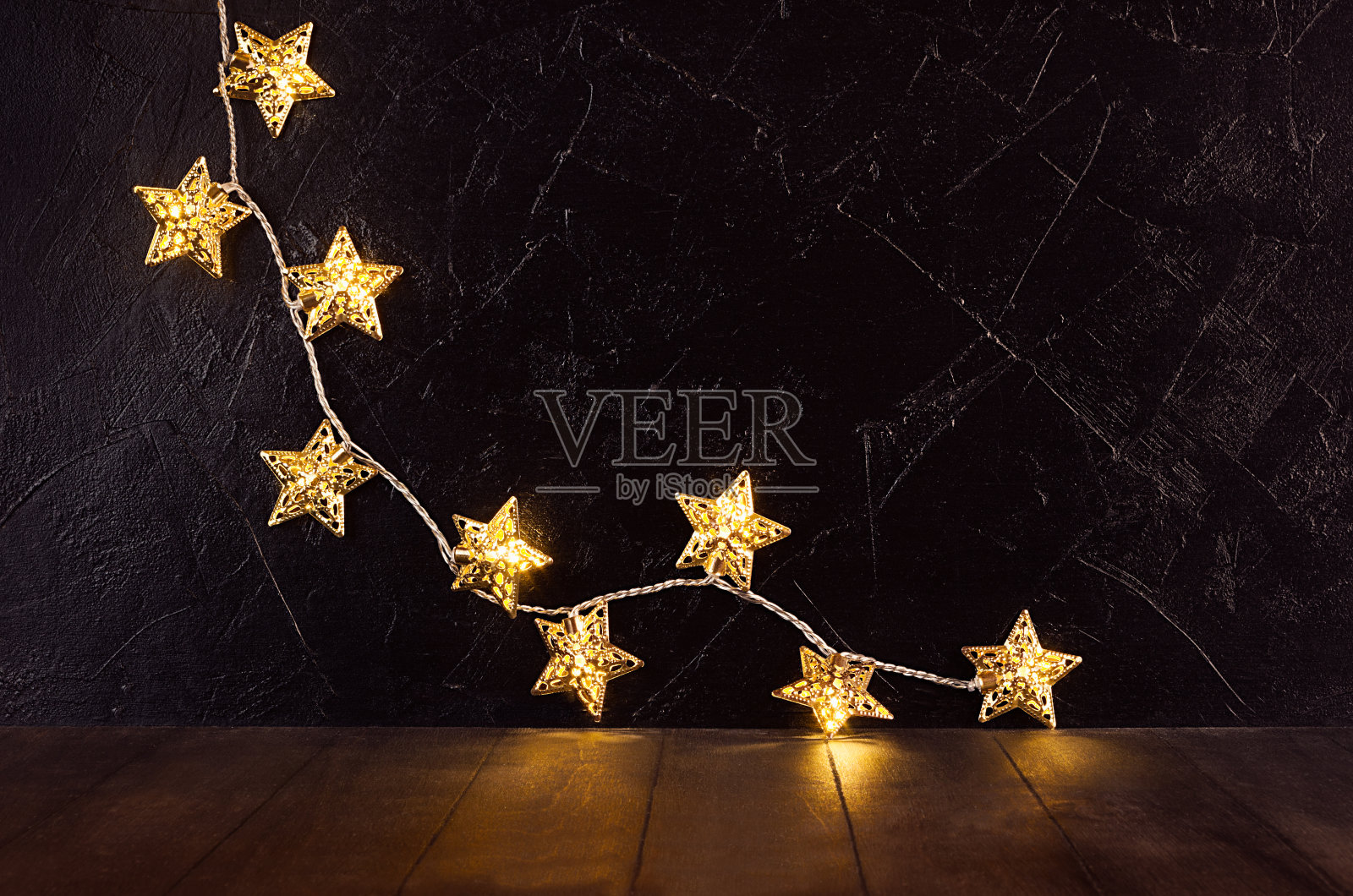 豪华的家庭装饰新年派对-条纹金色的圣诞发光灯与星星在优雅的黑暗内部在棕色的木头桌子，复印空间。照片摄影图片