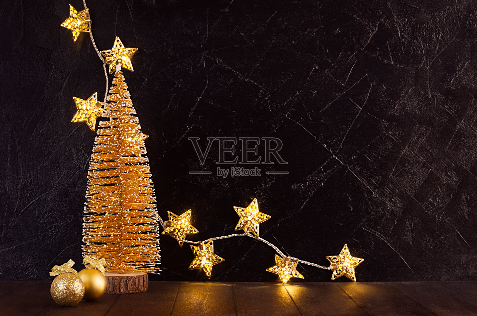 圣诞节日室内用金色的圣诞树，发光的灯与星星，装饰，闪闪发光的丝带在黑色的石膏墙和棕色的桌子，复制空间。照片摄影图片