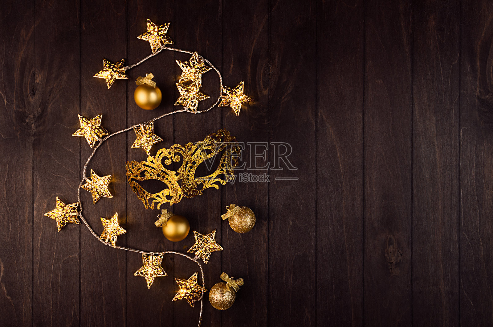 明亮的新年背景与金色华丽的闪光面具面具，星星发光的灯光在优雅的暗棕色板，俯视图。照片摄影图片