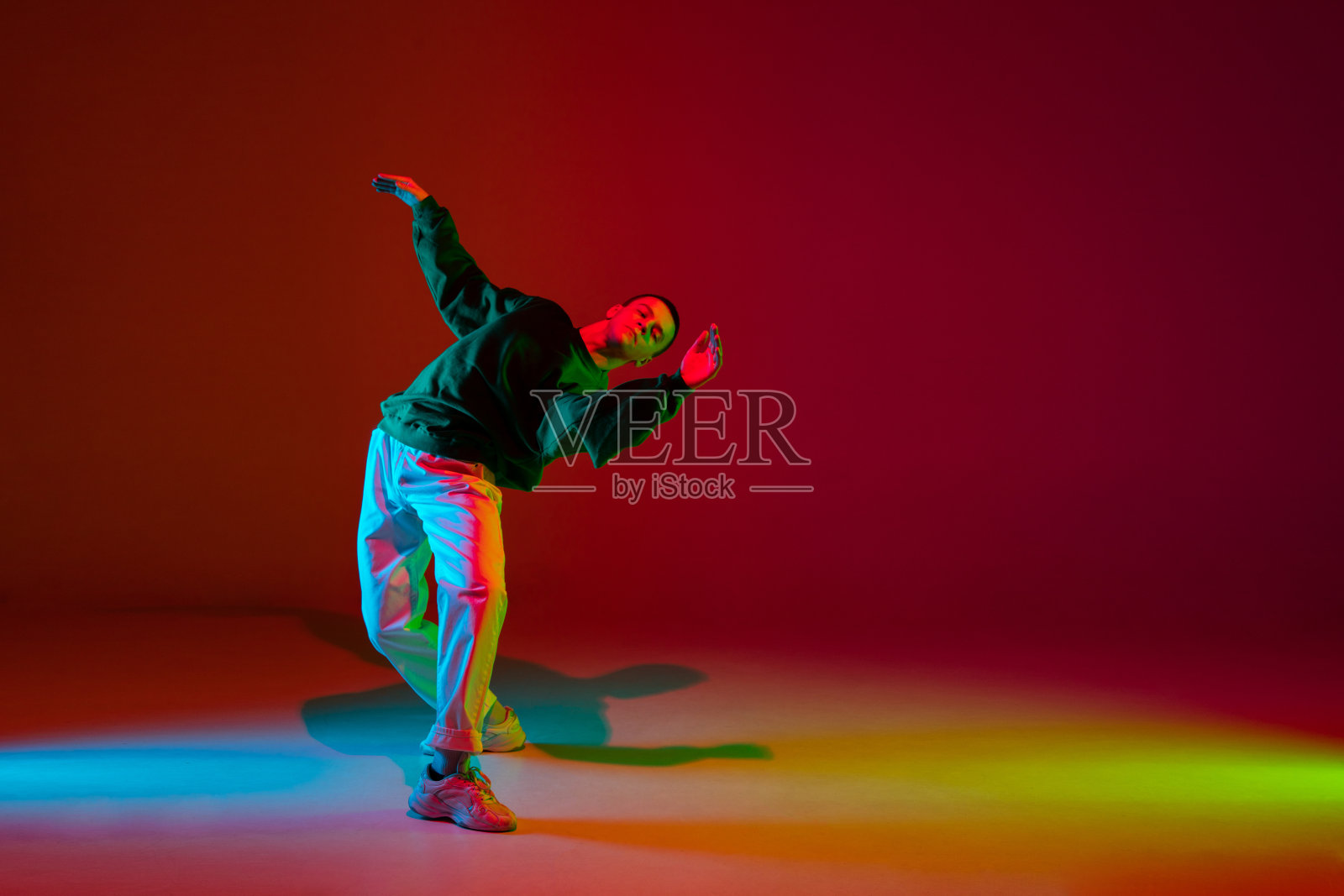 在霓虹灯下的舞厅里，时尚的运动男孩穿着时尚的衣服在五颜六色的背景下跳嘻哈舞。青年文化、运动、风格、时尚、行动。照片摄影图片