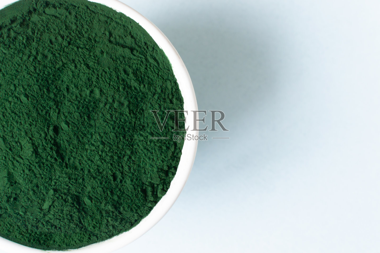 小球藻粉在一个白色的碗在蓝色的背景与文字的地方。照片摄影图片