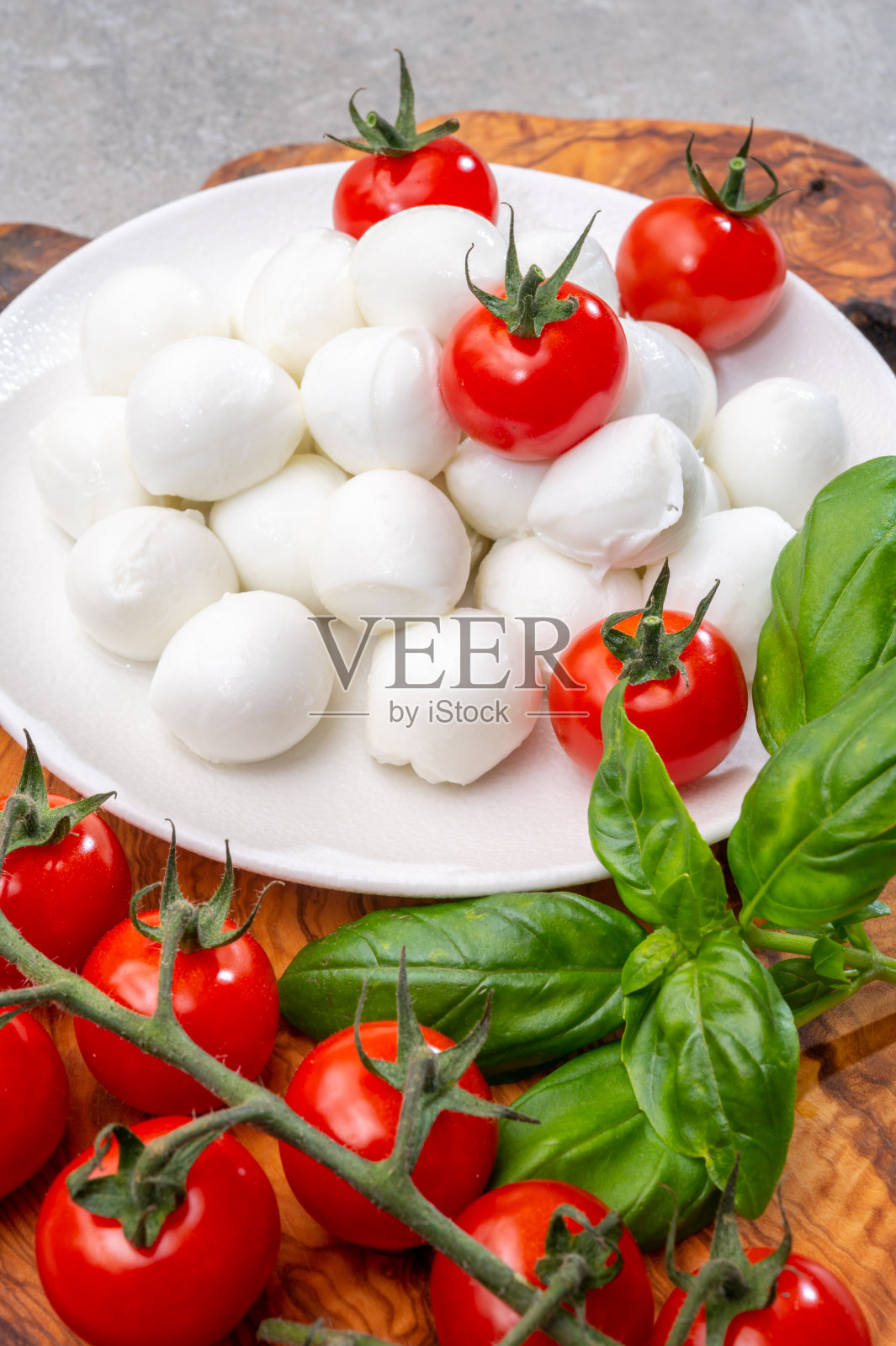 意大利三色奶酪，新鲜的白色软意大利马苏里拉奶酪小球，成熟的红色樱桃番茄和新鲜的绿色罗勒香草，准备做卡普里沙拉照片摄影图片