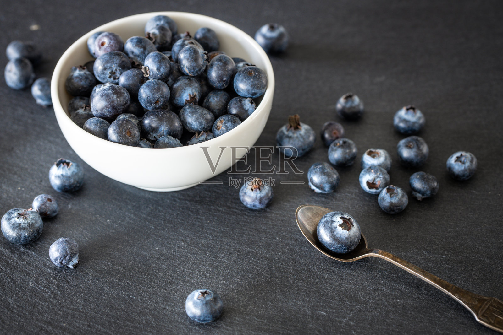 新鲜健康的蓝莓放在一个碗里，散落在黑色的石材台面上。放置你自己的题词照片摄影图片