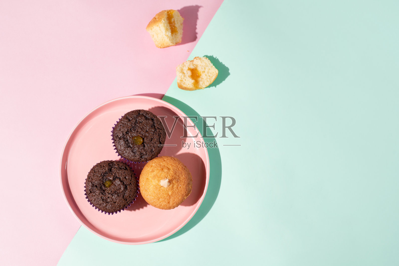 3个巧克力和香草松饼放在一个盘子上，粉红色和绿松石背景和面包屑。照片摄影图片