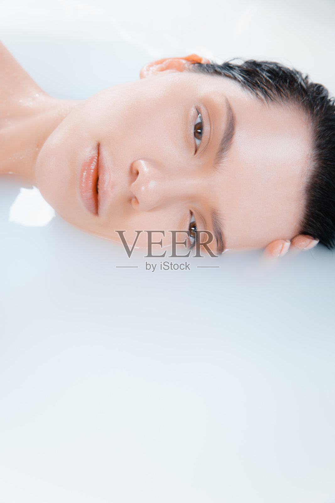 近距离的女性模特在牛奶浴与柔和的白色发光。Copyspace广告。美丽、时尚、风格、身体护理理念。照片摄影图片