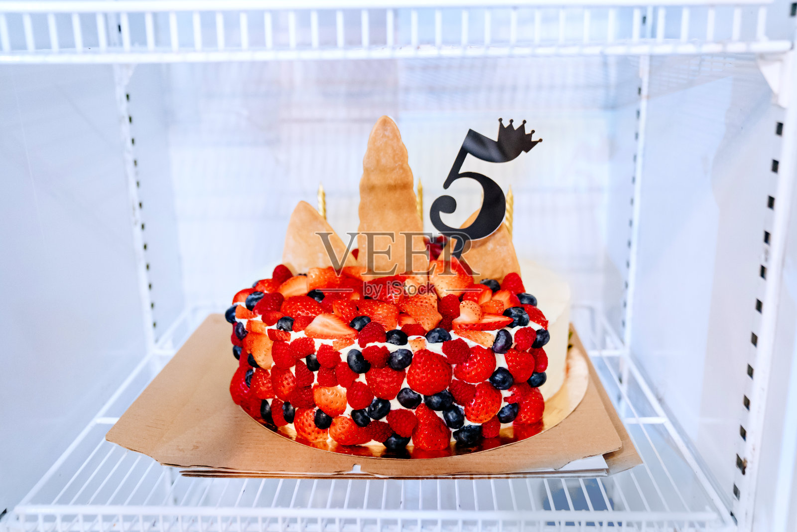 冰箱里有一个用浆果和数字5装饰的生日蛋糕。照片摄影图片