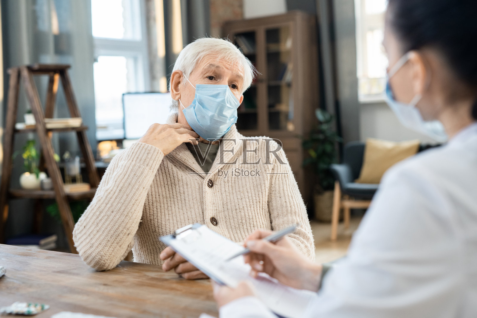 生病的资深男子穿着休闲服和防护面具与年轻的女医生交谈照片摄影图片