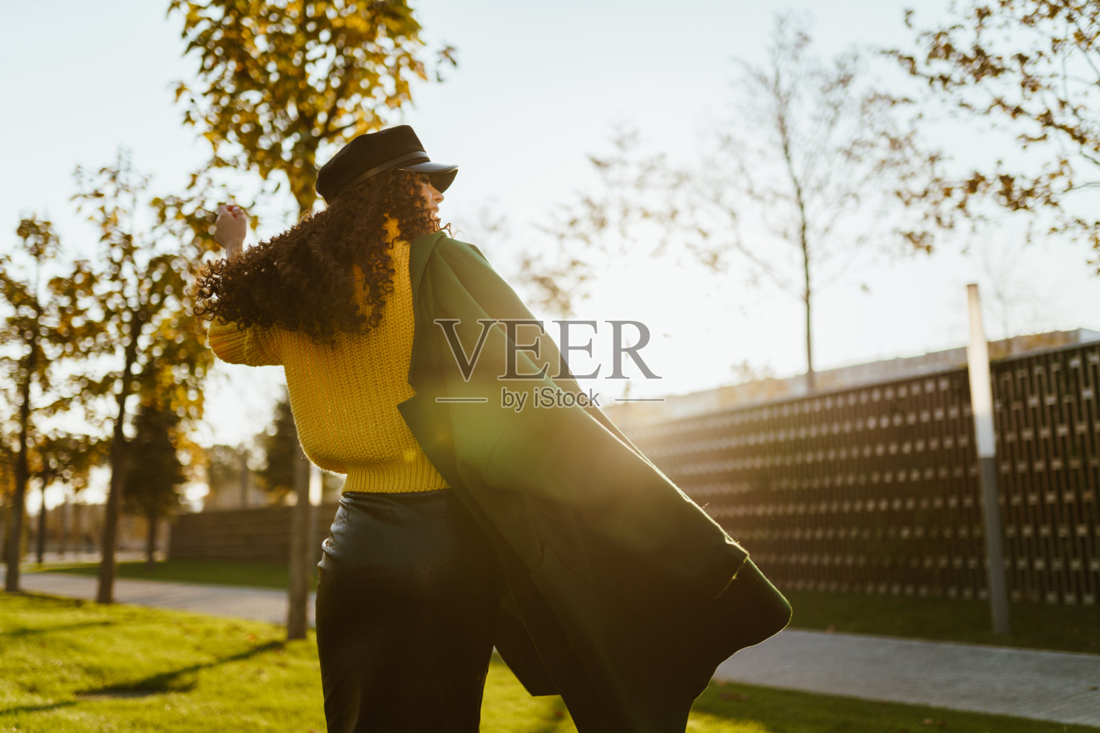 从后面看，一个女孩在秋天的公园里散步，肩上披着一件外套，夕阳西下照片摄影图片