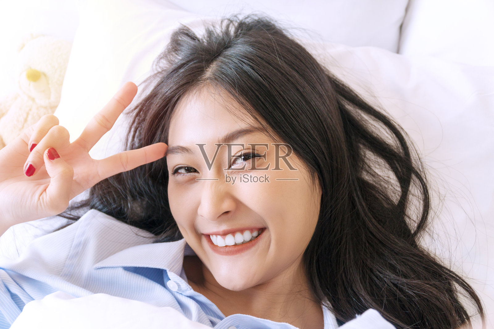 幸福微笑的年轻女子使用智能手机在床上自拍社交媒体。快乐的女孩躺在白色的床上用手机自拍早上在家里。生活方式放松的概念照片摄影图片