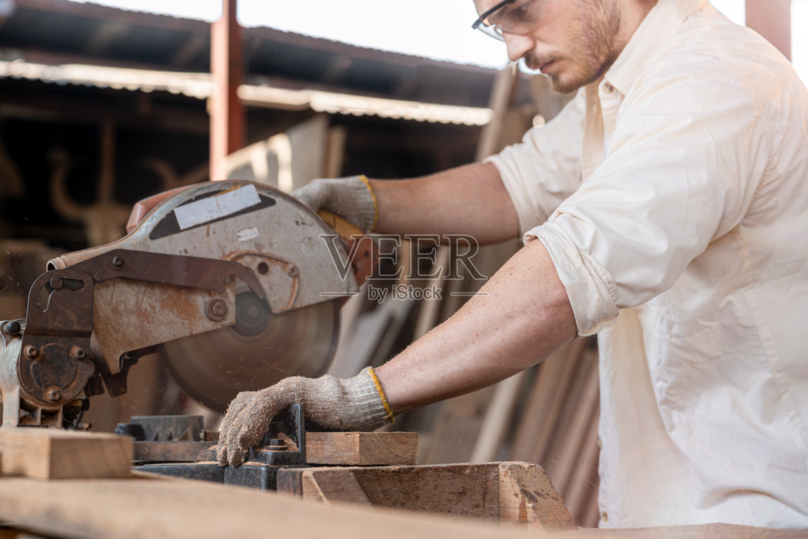 工人、木匠在工厂使用链锯机切割木制品。戴着眼罩保护锯末免受木头伤害的聪明人。工匠工作在木材车间工业。照片摄影图片