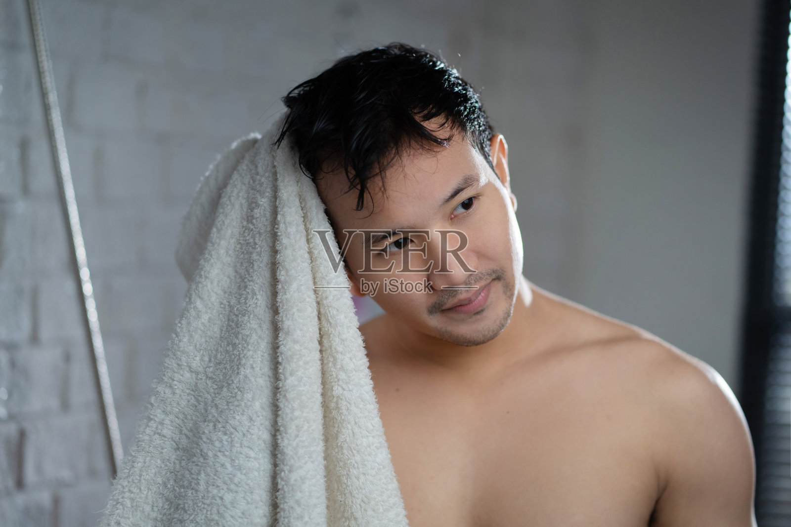 英俊的亚洲人洗完澡后在浴室里擦头。照片摄影图片