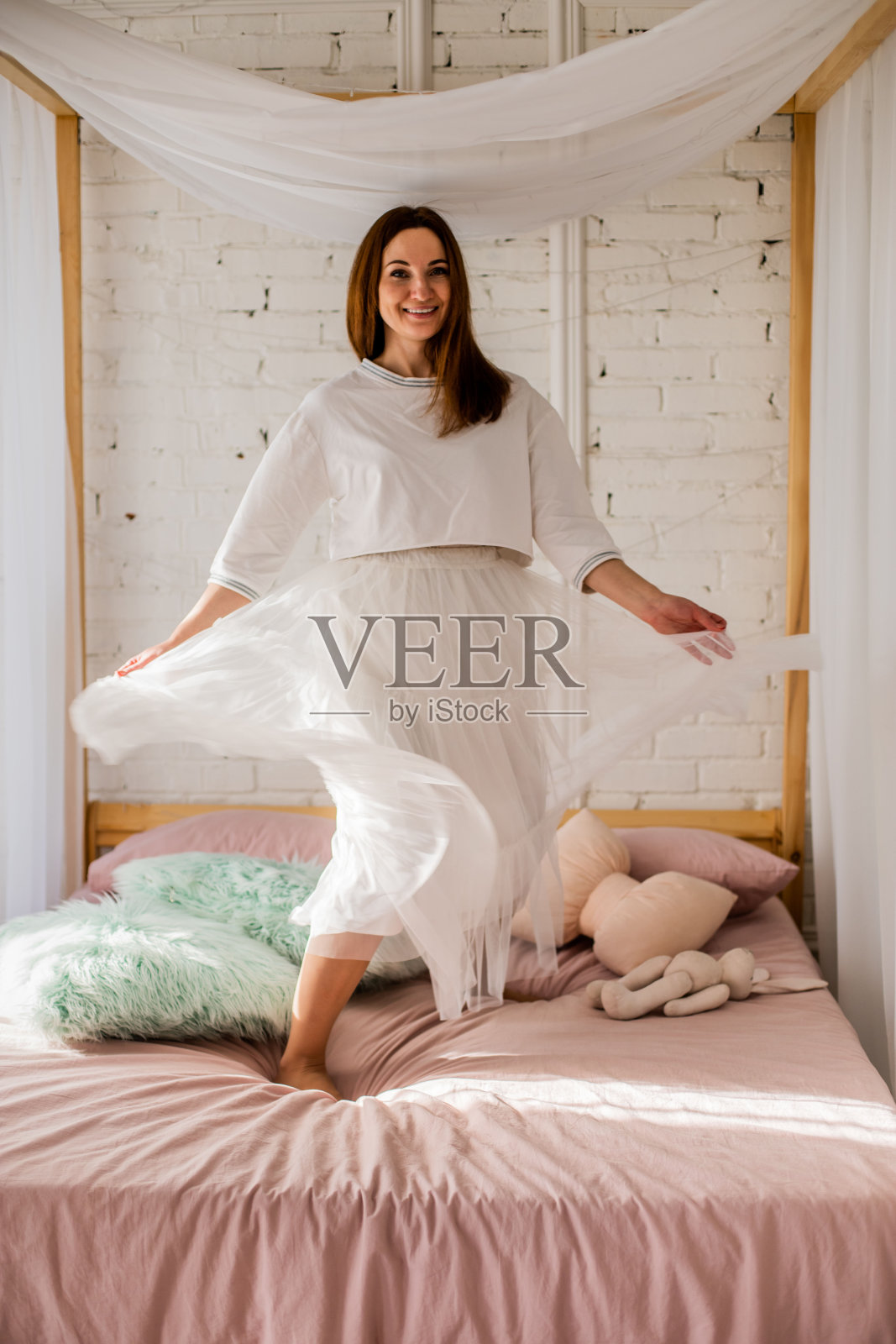 在阁楼卧室里，穿着白色短裙跳舞的快乐女士有着积极的情绪照片摄影图片