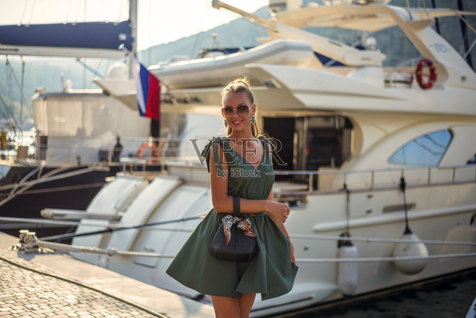 一个漂亮的女人穿着时髦的夏装和时尚的配件走在海滨长廊旁边昂贵的游艇照片摄影图片