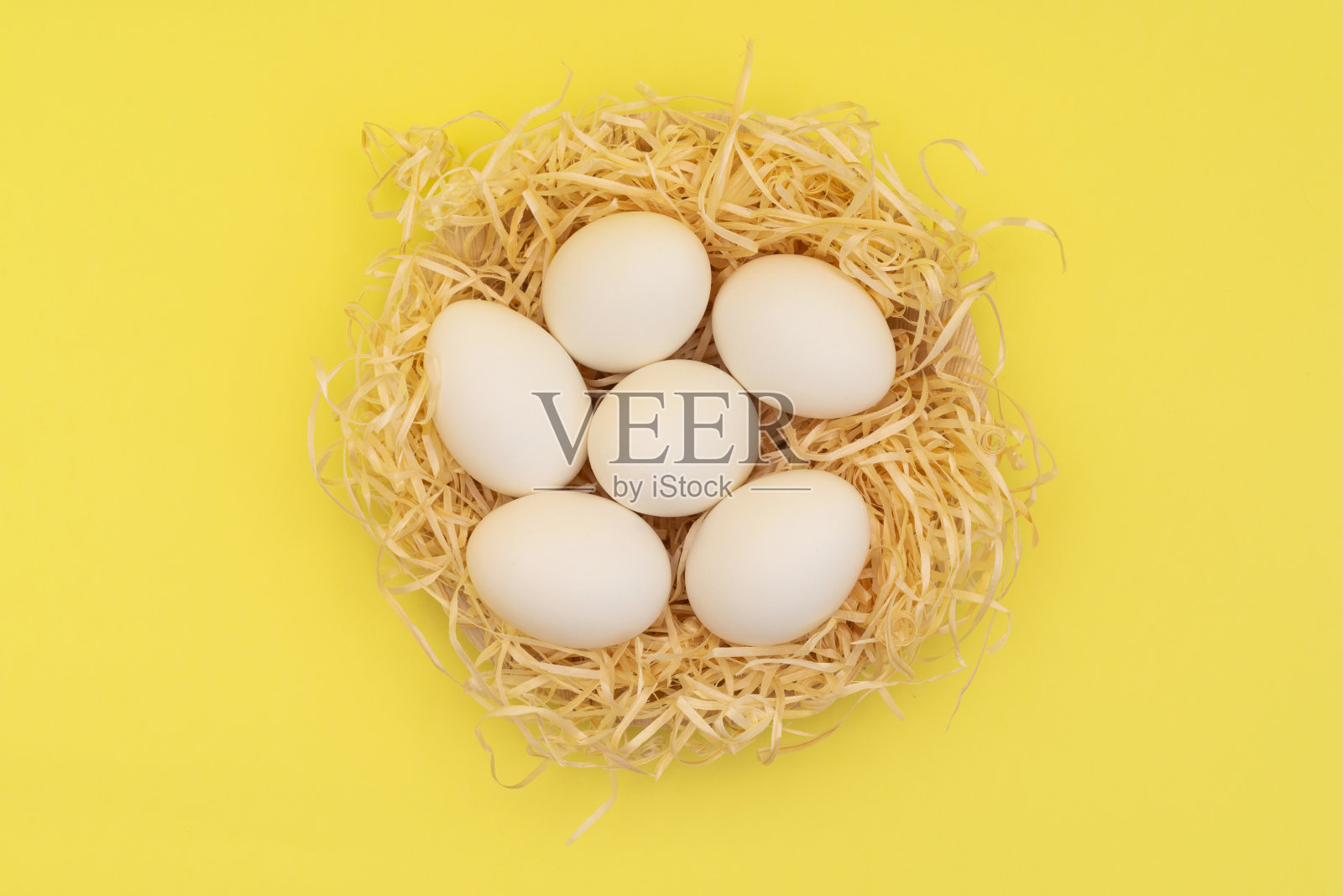 复活节白色的蛋在稻草窝在黄色的背景。复活节背景在照亮黄色2021年。俯视图照片摄影图片
