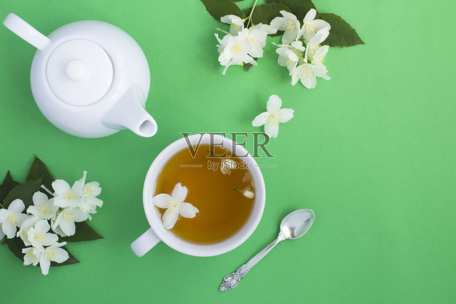 茉莉花绿茶在白色的茶杯，茶壶和花在绿色的背景照片摄影图片