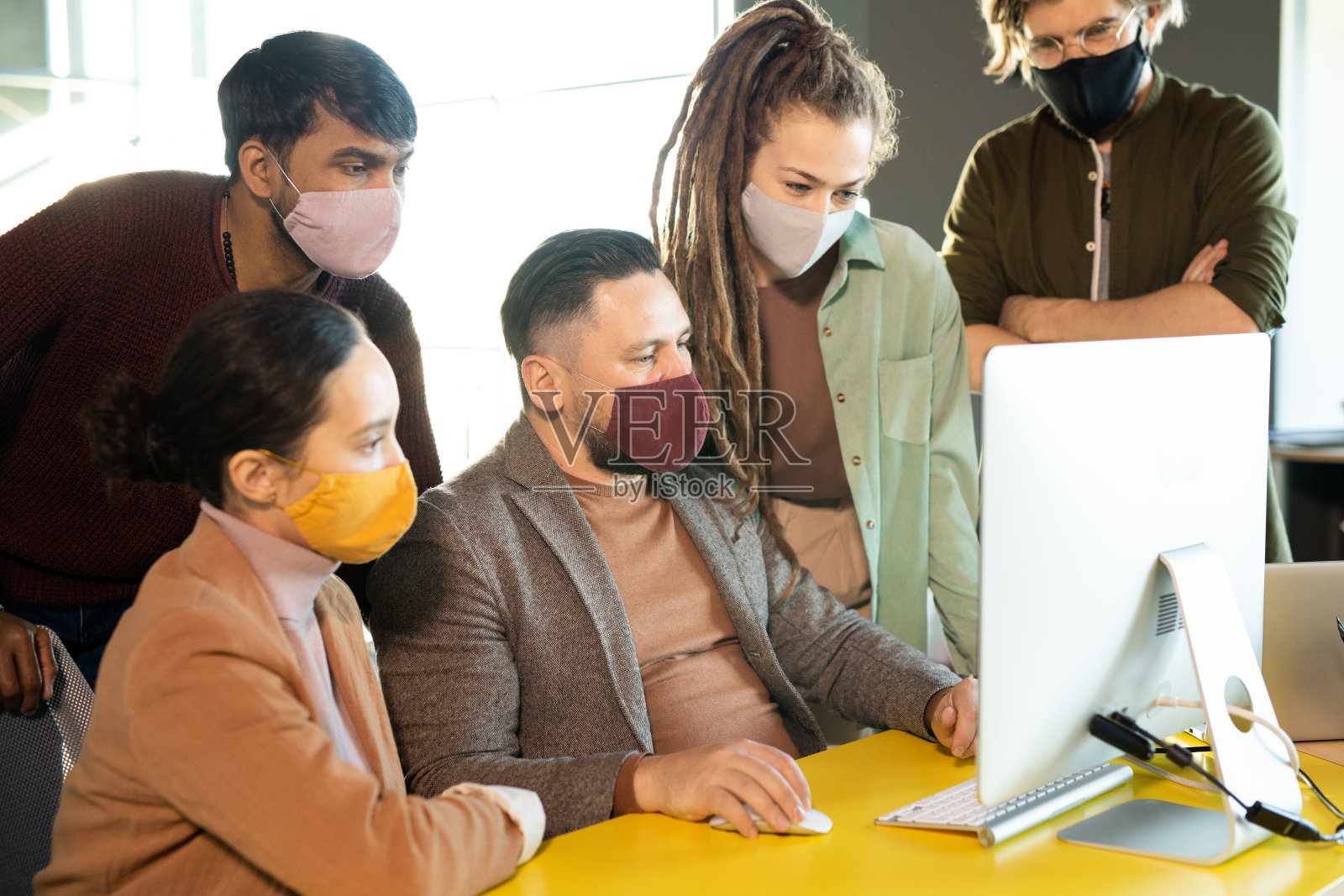 一群富有创意的年轻设计师聚集在电脑显示器前的桌子旁照片摄影图片