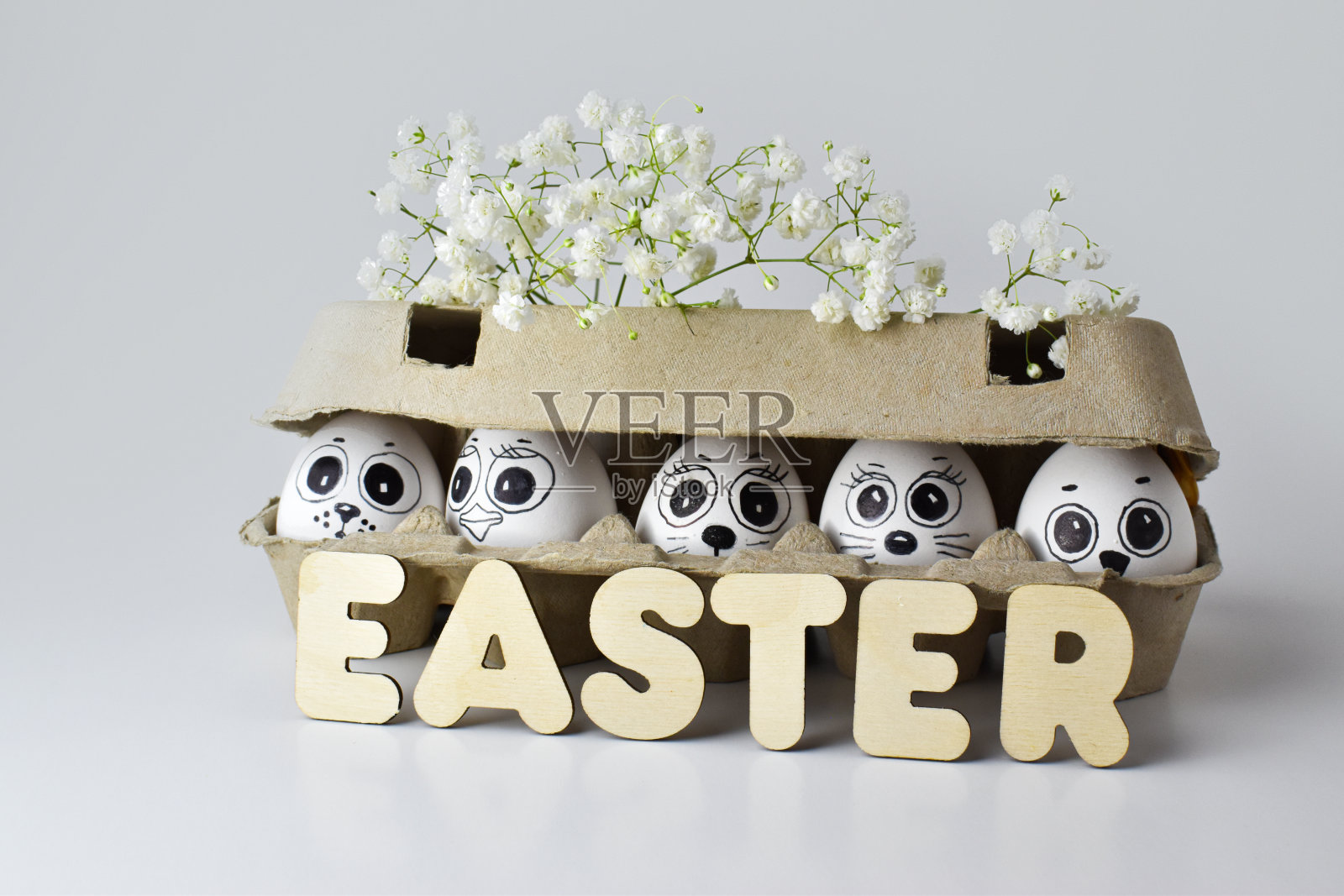 一盒鸡蛋，在明亮的背景上有人脸和花。复活节装饰品。隐藏的鸡蛋。照片摄影图片