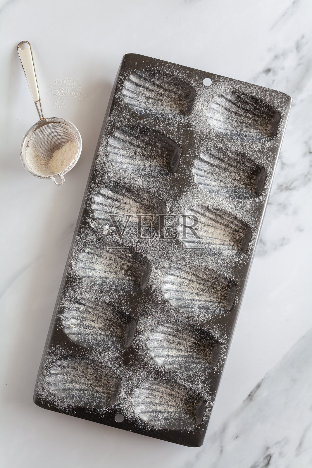 从上往下看，一个抹了油和面粉的玛德琳蛋糕烤盘，对角线，筛子铺在白色大理石背景上照片摄影图片