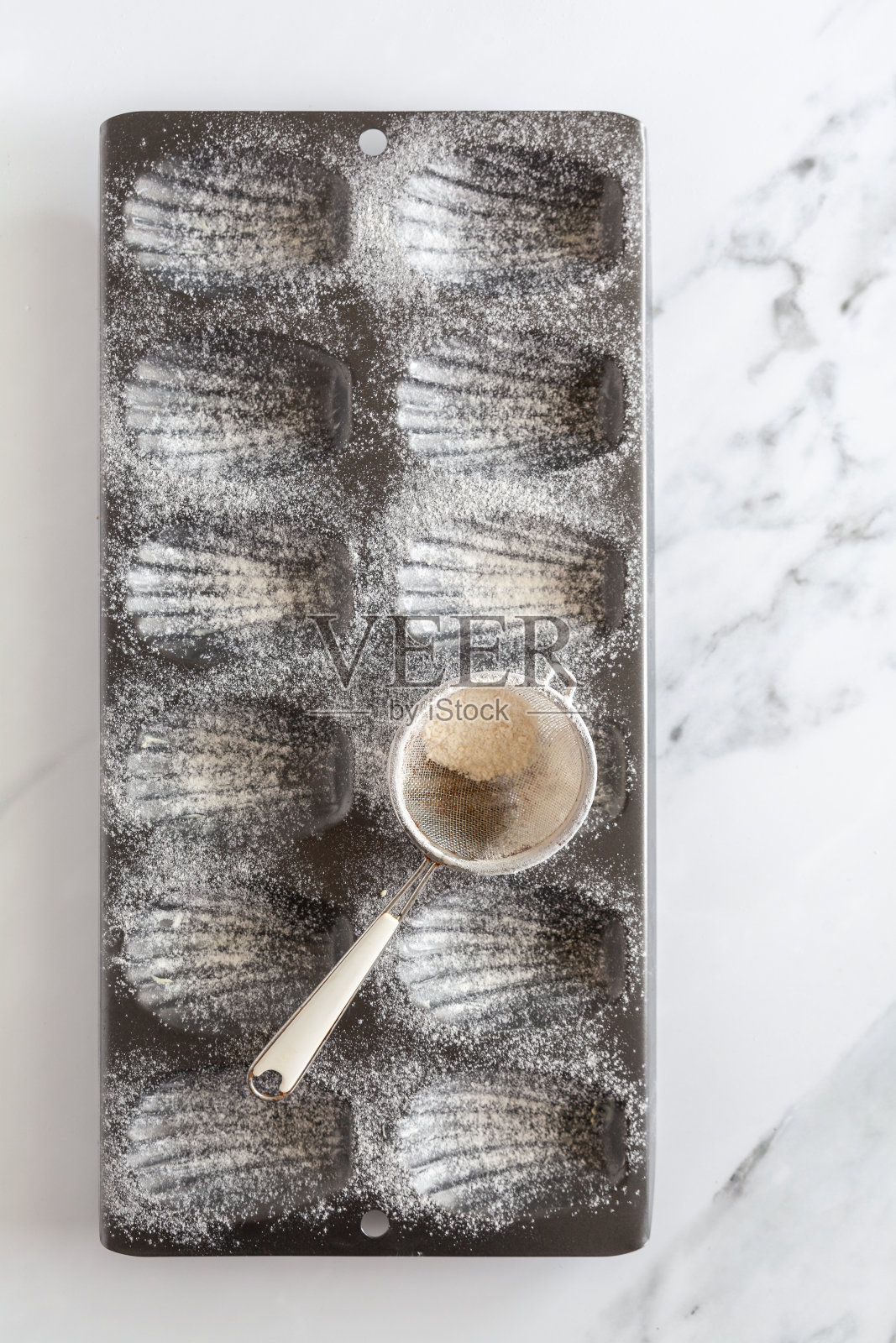 从上往下看，一个抹了油和面粉的玛德琳蛋糕烤盘，筛子铺在白色大理石背景上照片摄影图片