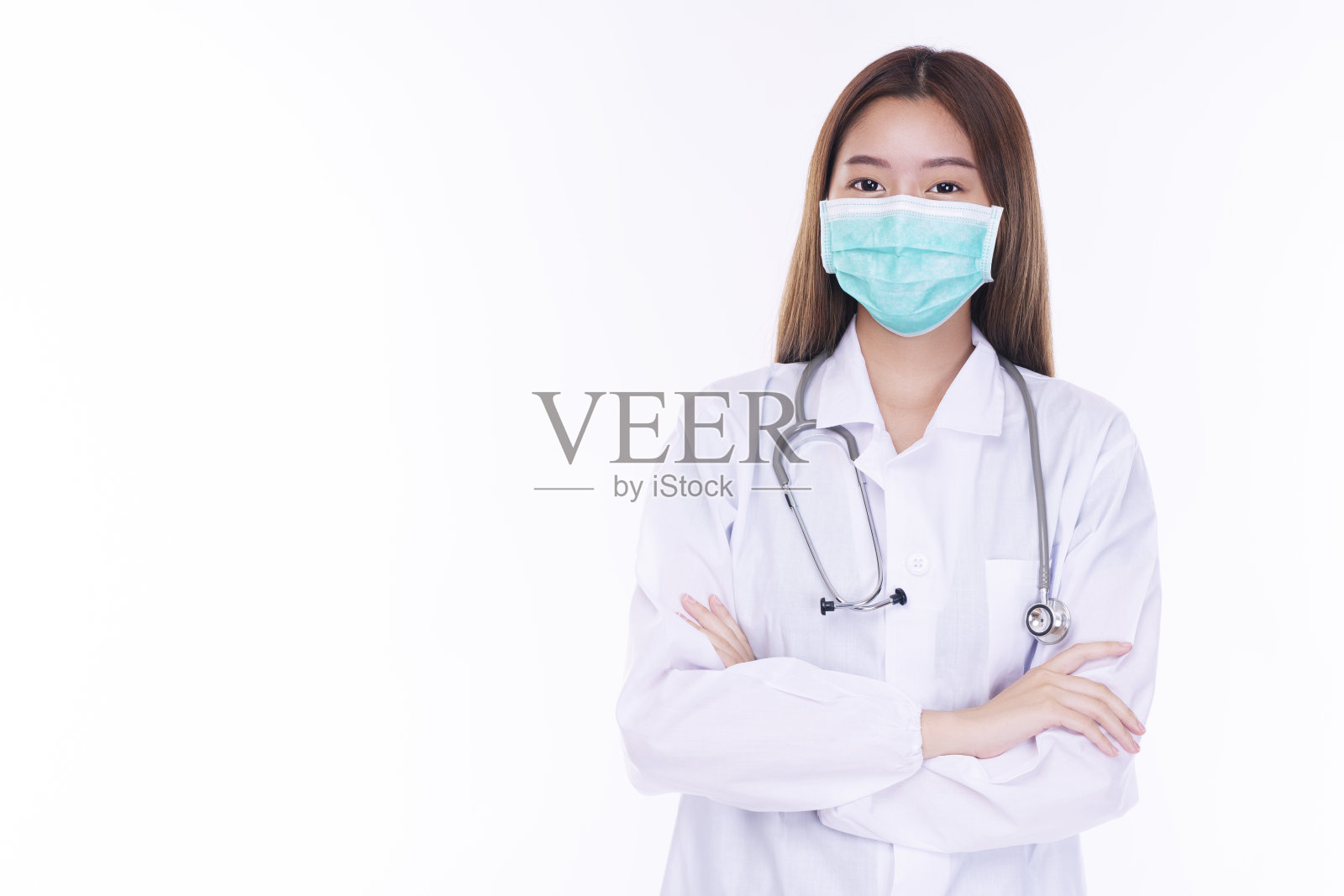 专业的年轻女医生穿着大衣制服与听诊器手臂交叉看着相机，而站在孤立的白色背景微笑。健康保健和保险理念。照片摄影图片