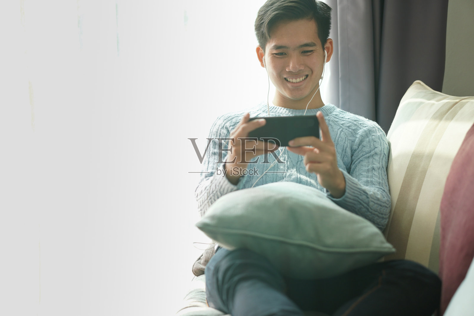 一名亚洲男子戴着耳机用智能手机听音乐，躺在家里的沙发上休息照片摄影图片