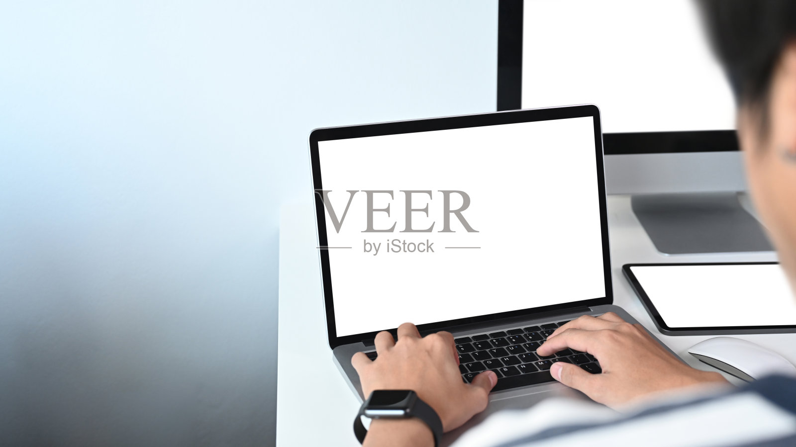 一个年轻人在笔记本电脑上工作，使用多种现代设备。照片摄影图片