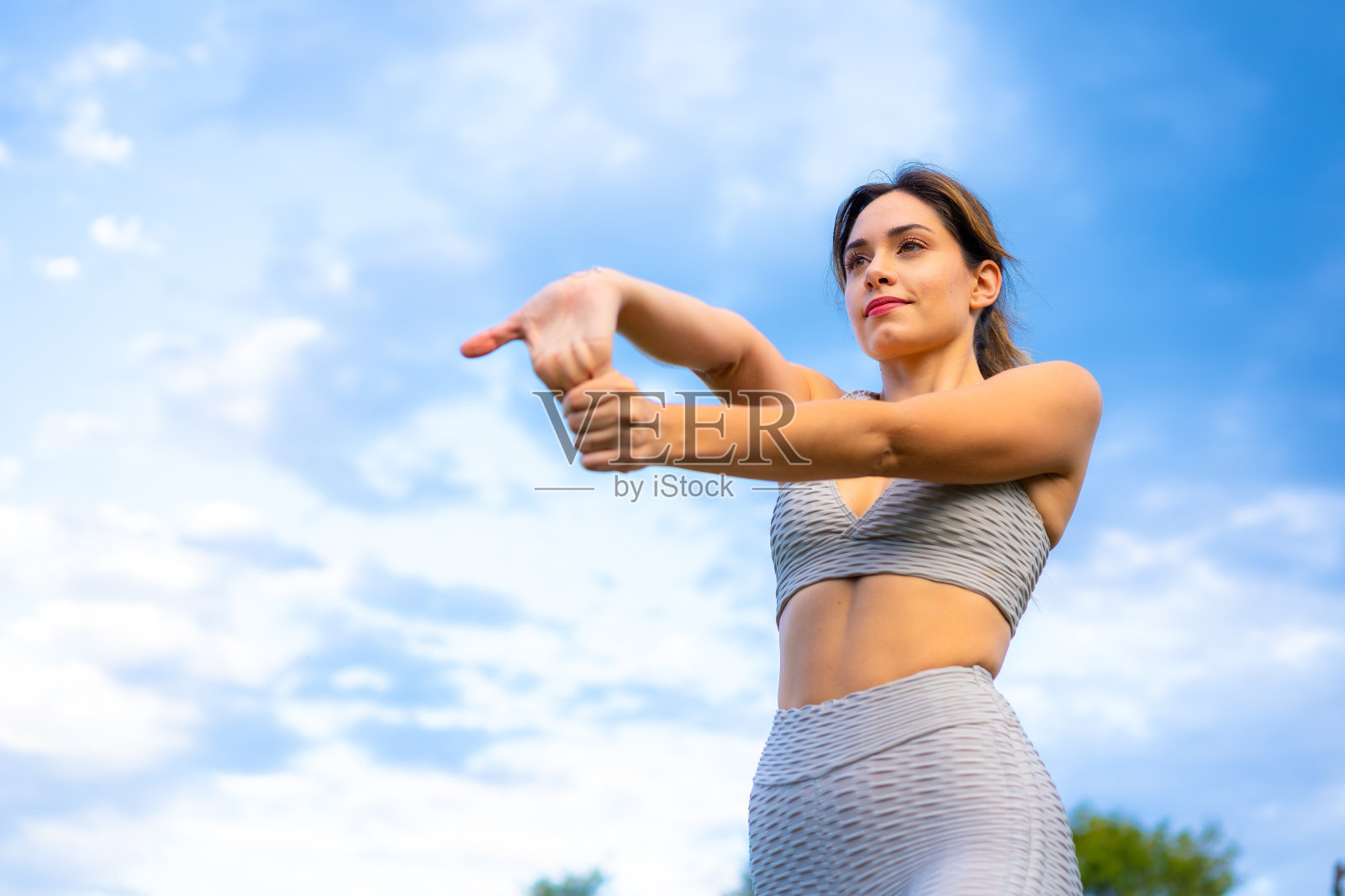 一个年轻的金发白种人健身，非常欢快地做着伸展运动，以天空为背景，在操场上锻炼，灰色的运动服，健康的女孩，健康的生活照片摄影图片