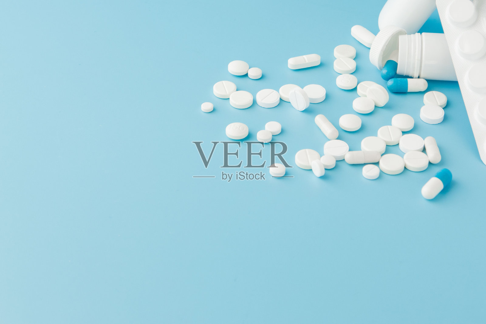 蓝色背景上散落着各种药片、药品、喷雾、瓶子、温度计、注射器和空的购物车。药房购物的概念照片摄影图片