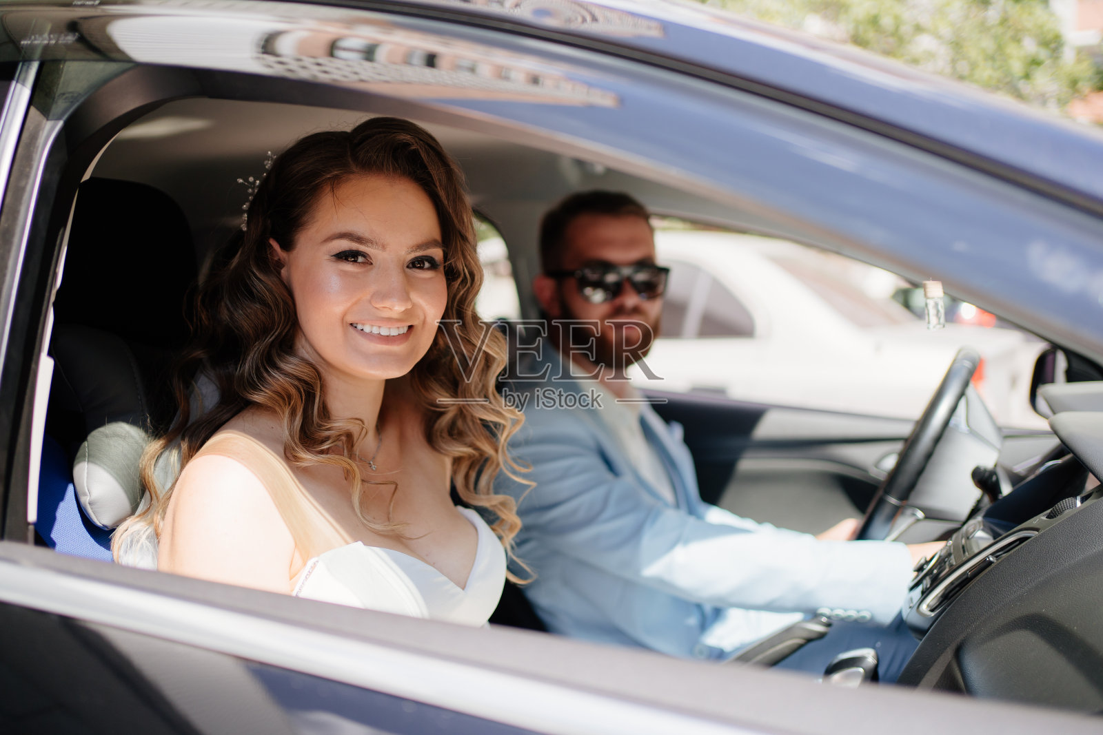 新郎穿着蓝色西装，新娘穿着优雅的白色礼服，捧花坐在黑色的车里照片摄影图片