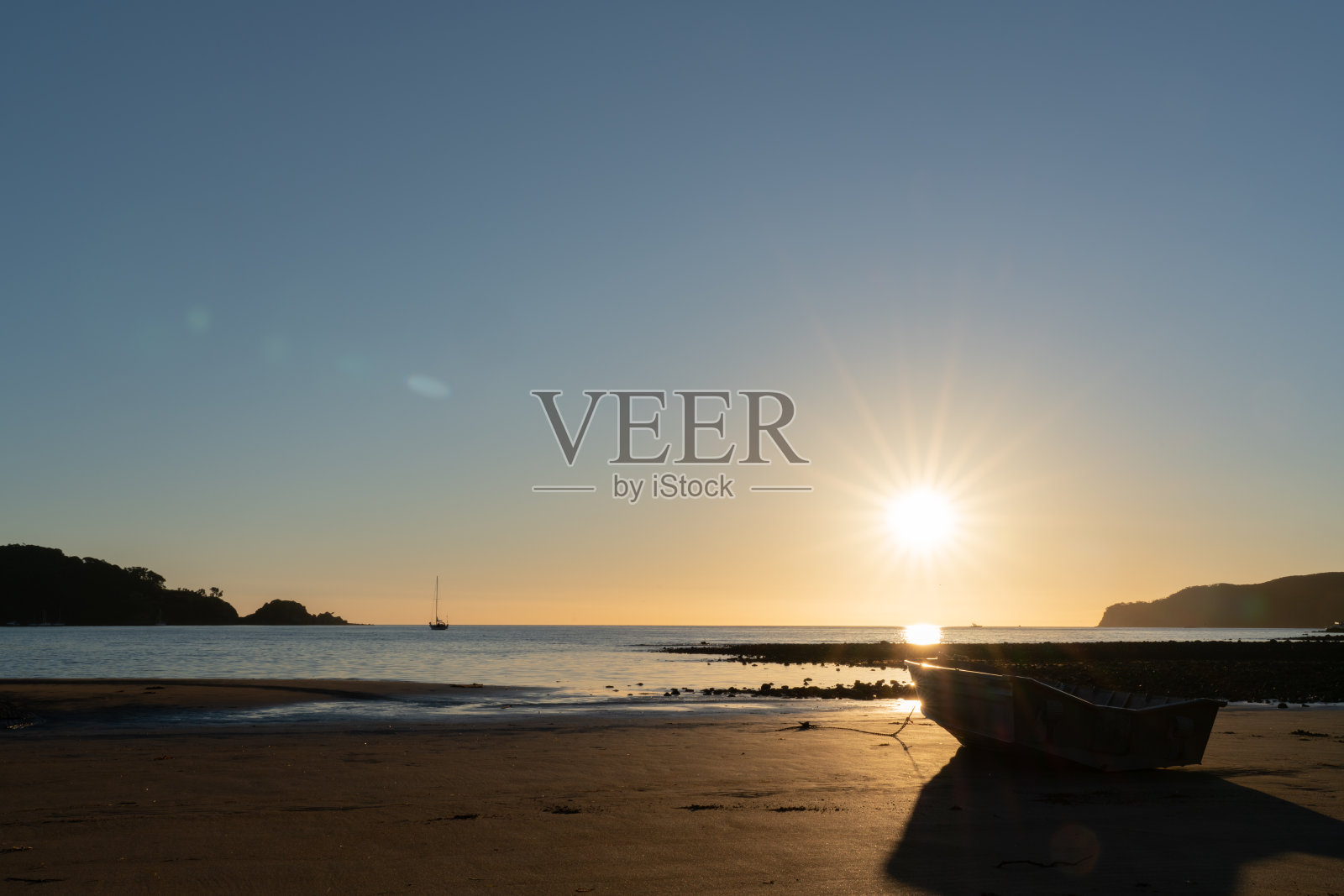 低潮时坐在沙地上的小船在落日的背景下形成了一个剪影。照片摄影图片