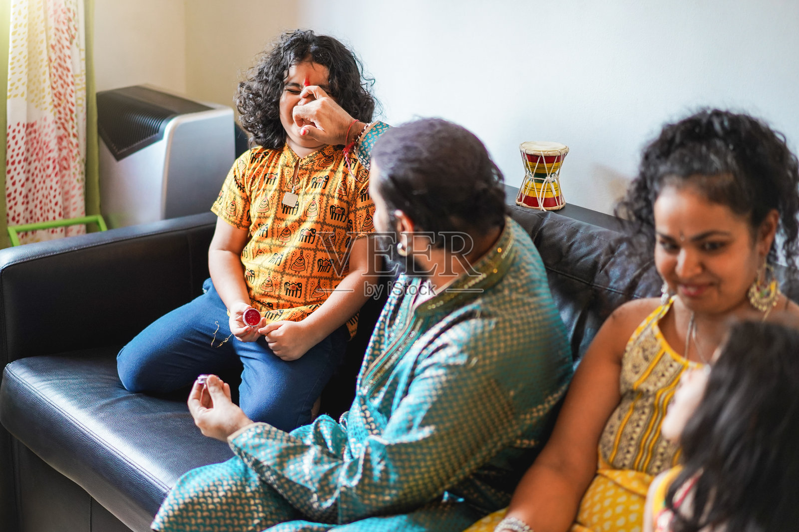 快乐的印度家庭坐在沙发上玩得开心-关注母亲照片摄影图片