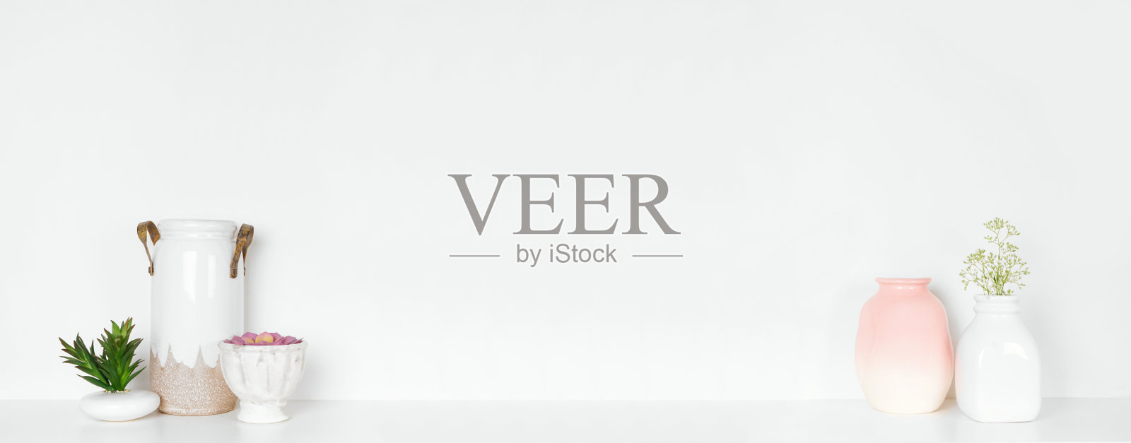 架子上的家居装饰。现代花瓶，多肉植物和鲜花。白色的架子靠着白色的墙。照片摄影图片