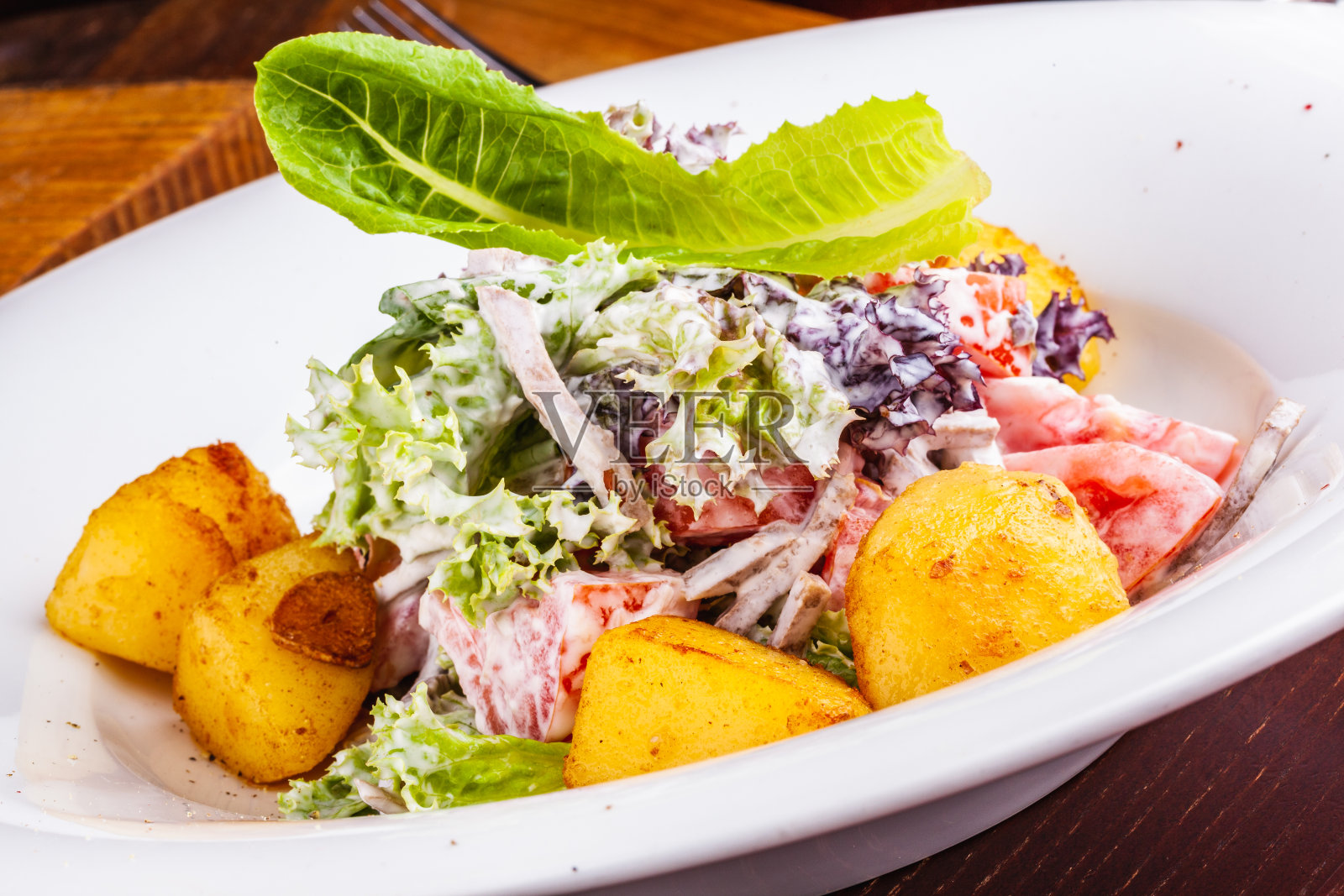 配烤土豆、蕃茄、生菜和牛舌的沙拉放在白盘子里照片摄影图片