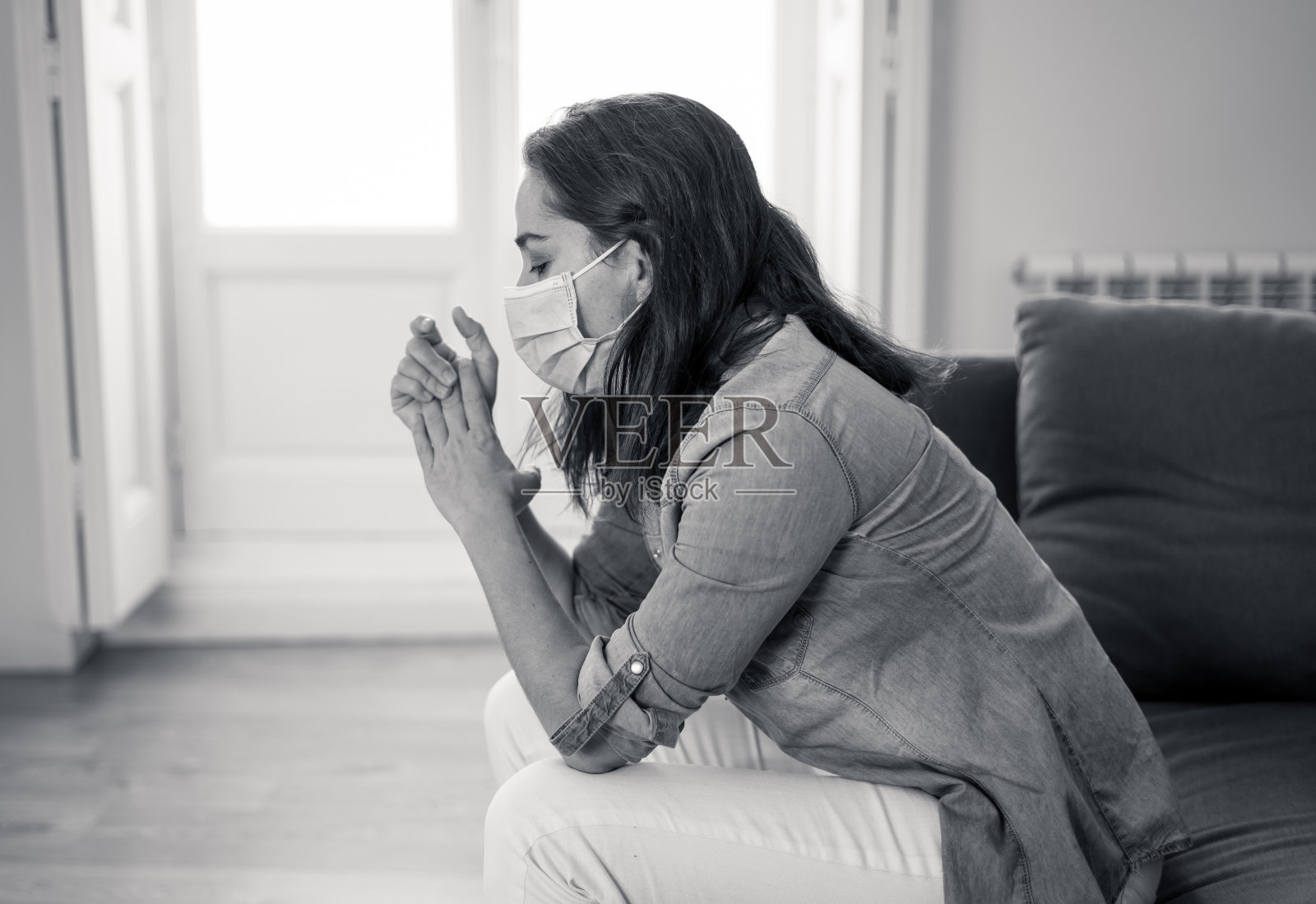 悲伤生病的拉丁女人戴着保护面罩沮丧在家里的沙发上。在冠状病毒死亡、禁闭和社交距离中，绝望的女性感到疲倦和担忧，遭受抑郁。心理健康和隔离概念。照片摄影图片