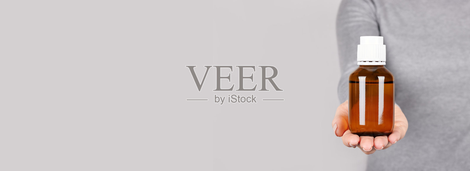 手拿药瓶，灰色背景。照片摄影图片