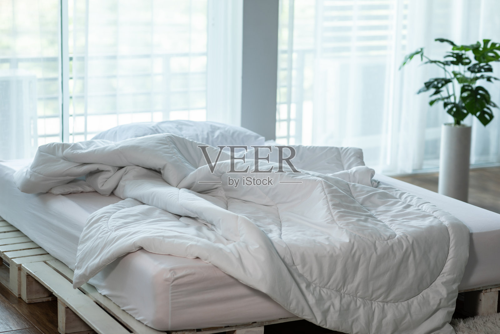 凌乱的床与白色的枕头和羽绒被毯与自然光在卧室早上，凌乱的床后，凌乱的床和舒适的卧室概念照片摄影图片