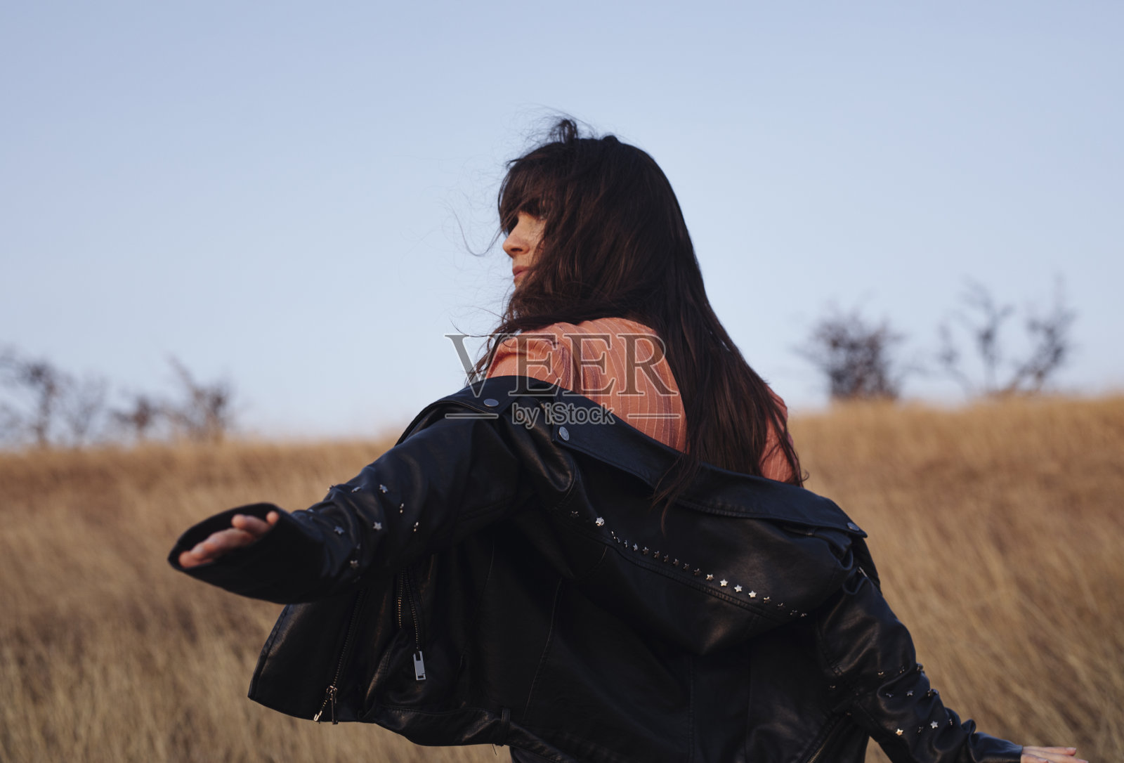 美丽的年轻女子穿着皮夹克享受风在高草地照片摄影图片