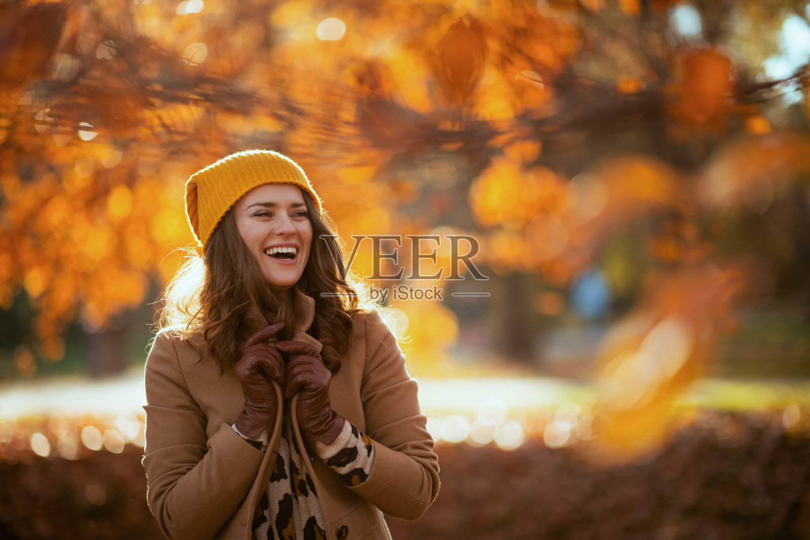 穿着米色外套，戴着橙色帽子的快乐时尚女性照片摄影图片