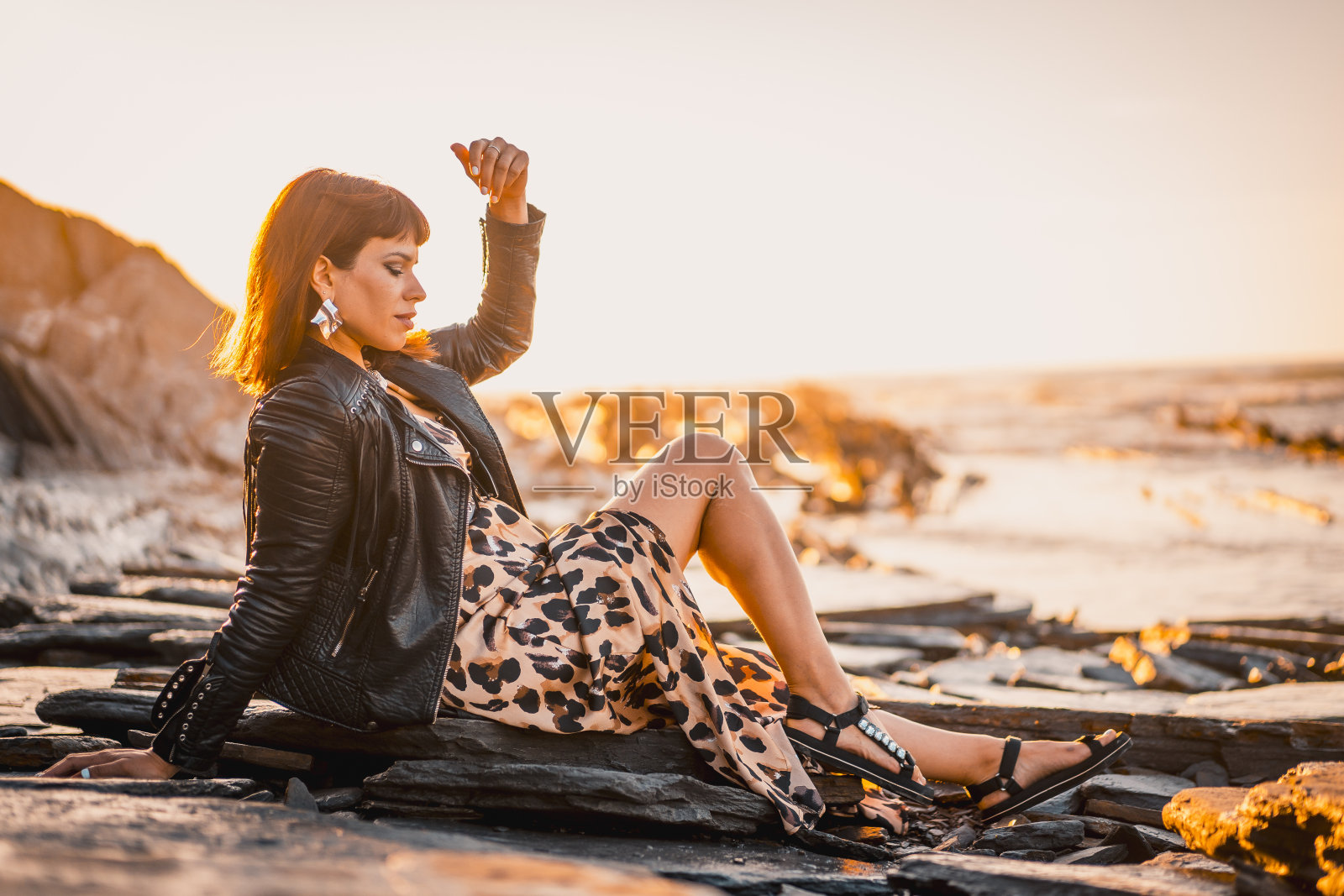 夏天的街头风格在海滩旁边的岩石一个年轻的黑发白种女人穿着豹纹裙的海边。巴斯克地区德巴镇的萨科内塔海滩。向右看照片摄影图片