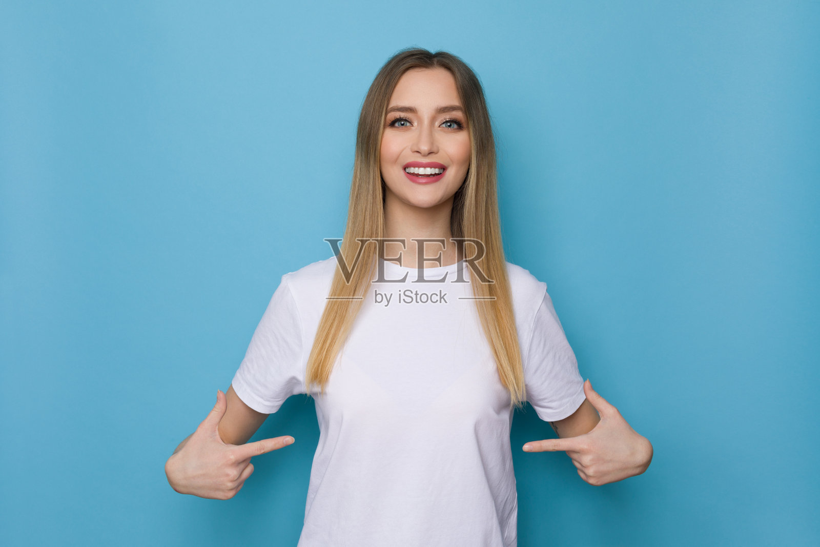 微笑的女孩指着她的白衬衫照片摄影图片