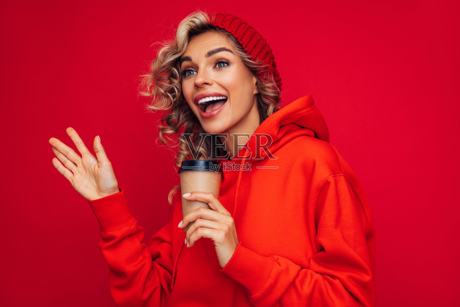 快乐的年轻愉快的女孩拿着一杯咖啡在彩色的红色背景照片摄影图片