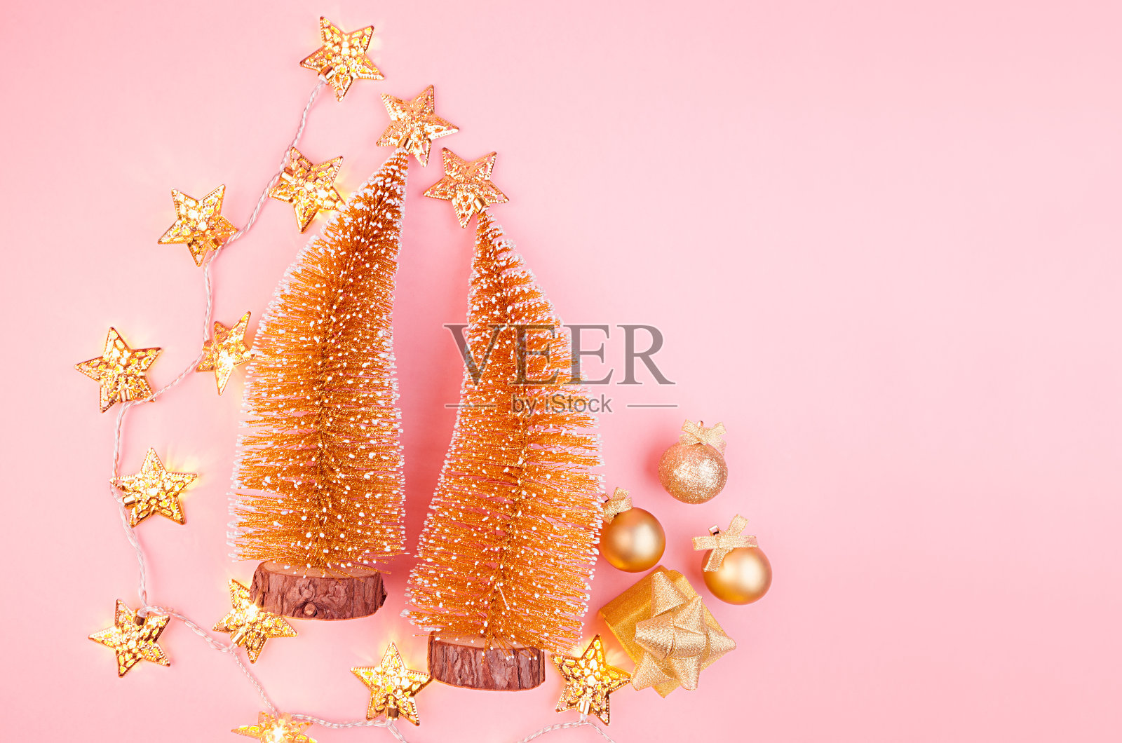 圣诞装饰在金色-圣诞树，发光的花环，星星在柔和的淡粉色背景，俯视图。照片摄影图片