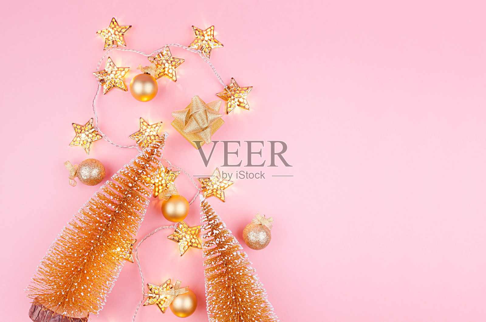 圣诞背景在金色闪光的颜色-圣诞树，球，礼物盒和发光的星星灯在浅粉色的背景，平lay。照片摄影图片