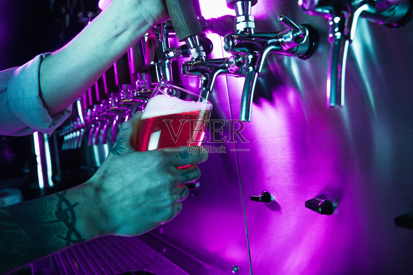 近距离的啤酒杯在酒吧侍者的手在五颜六色的霓虹灯。照片摄影图片