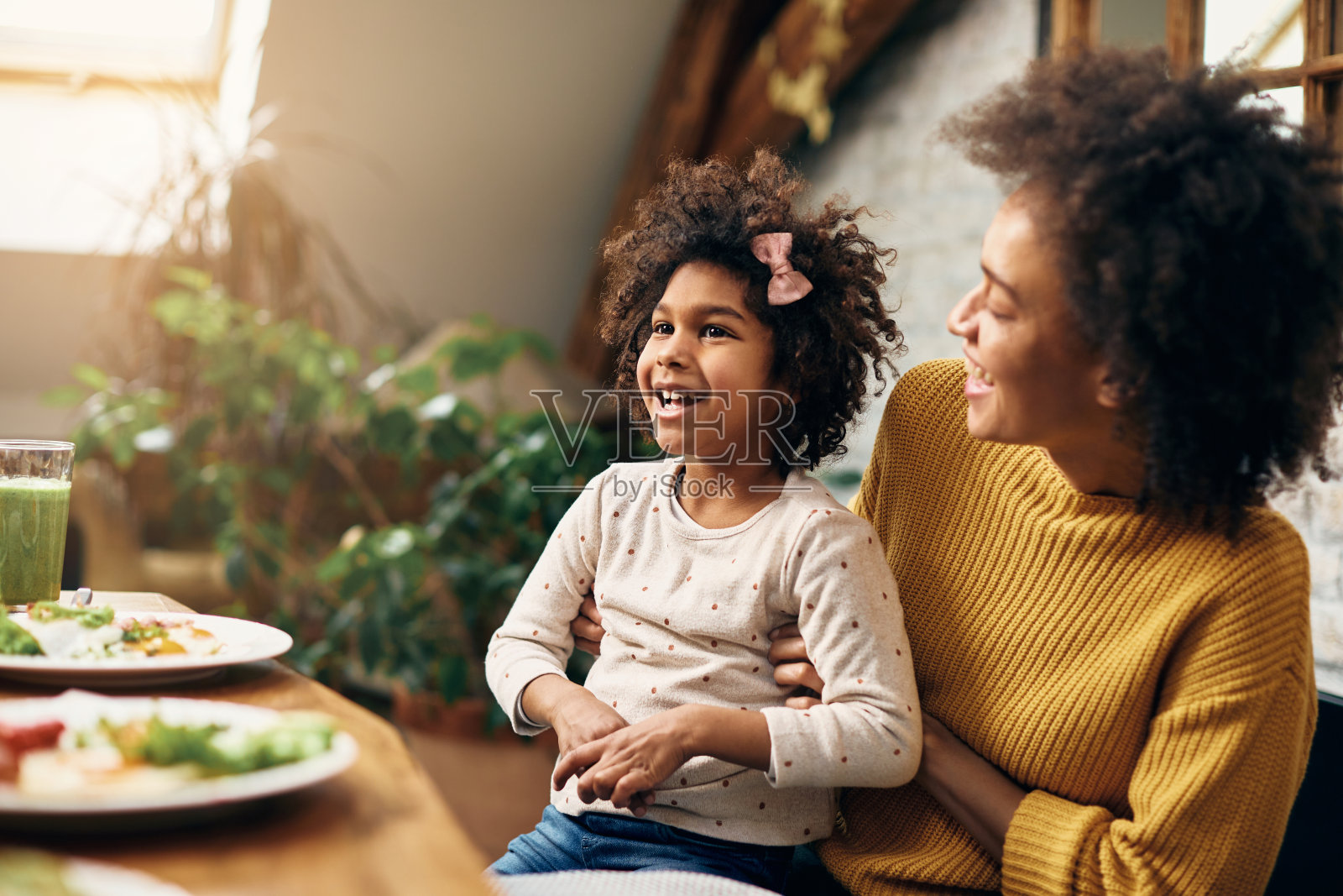 快乐的非洲裔美国女孩与她的母亲在餐桌上玩得开心。照片摄影图片