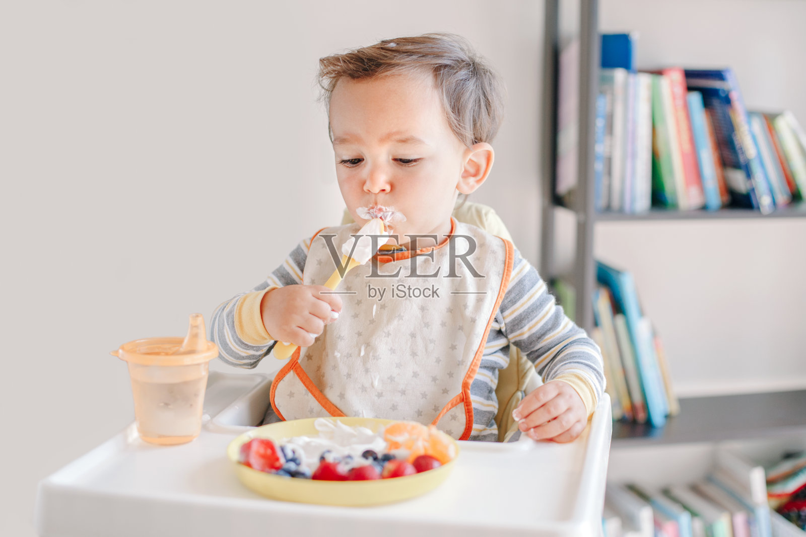 可爱的白人小男孩吃成熟的浆果和水果配酸奶。有趣的微笑的孩子坐在椅子上吃新鲜的浆果和喝水。幼儿的补充健康食品。照片摄影图片