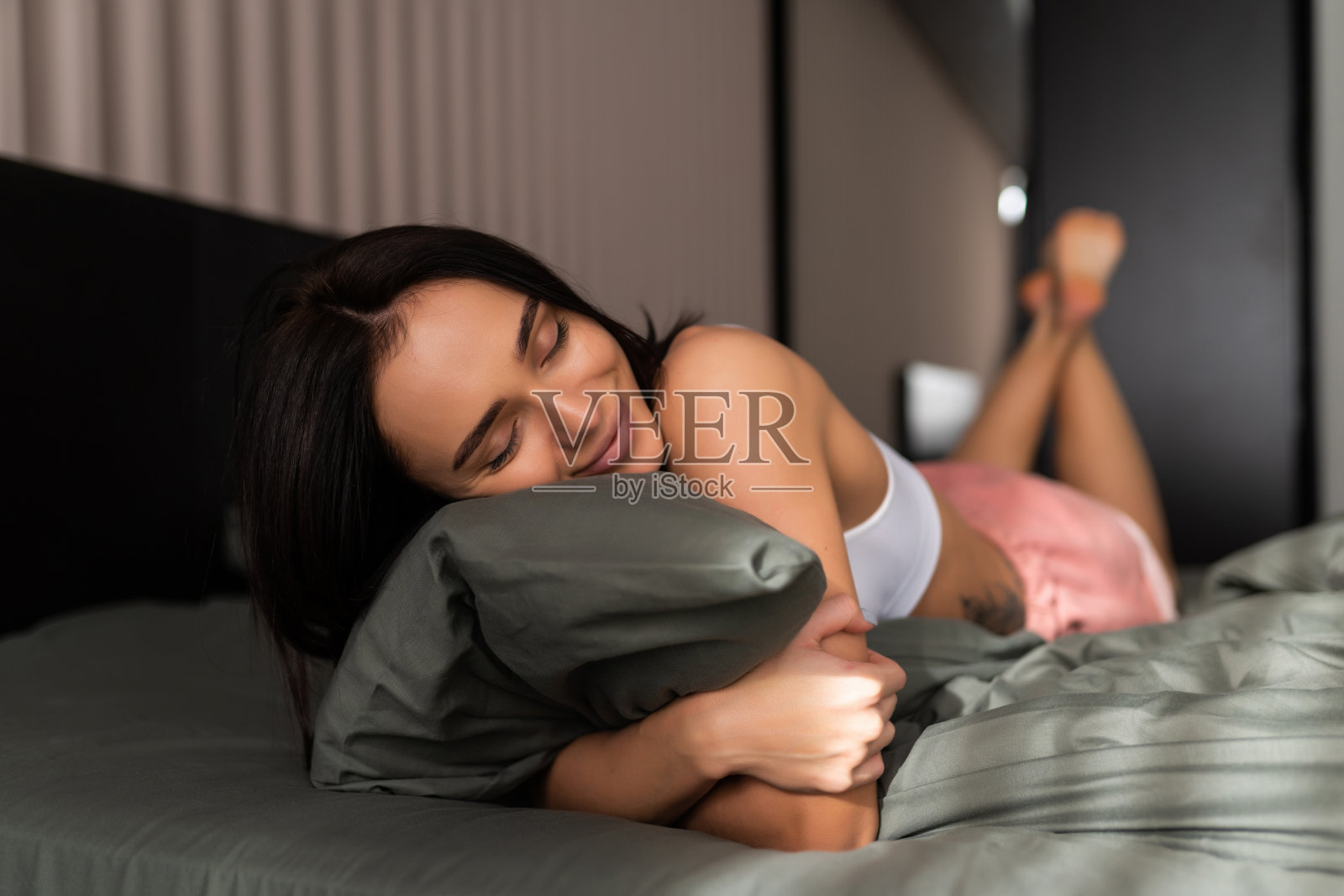 年轻美丽的女人微笑着躺在床上抱着枕头照片摄影图片