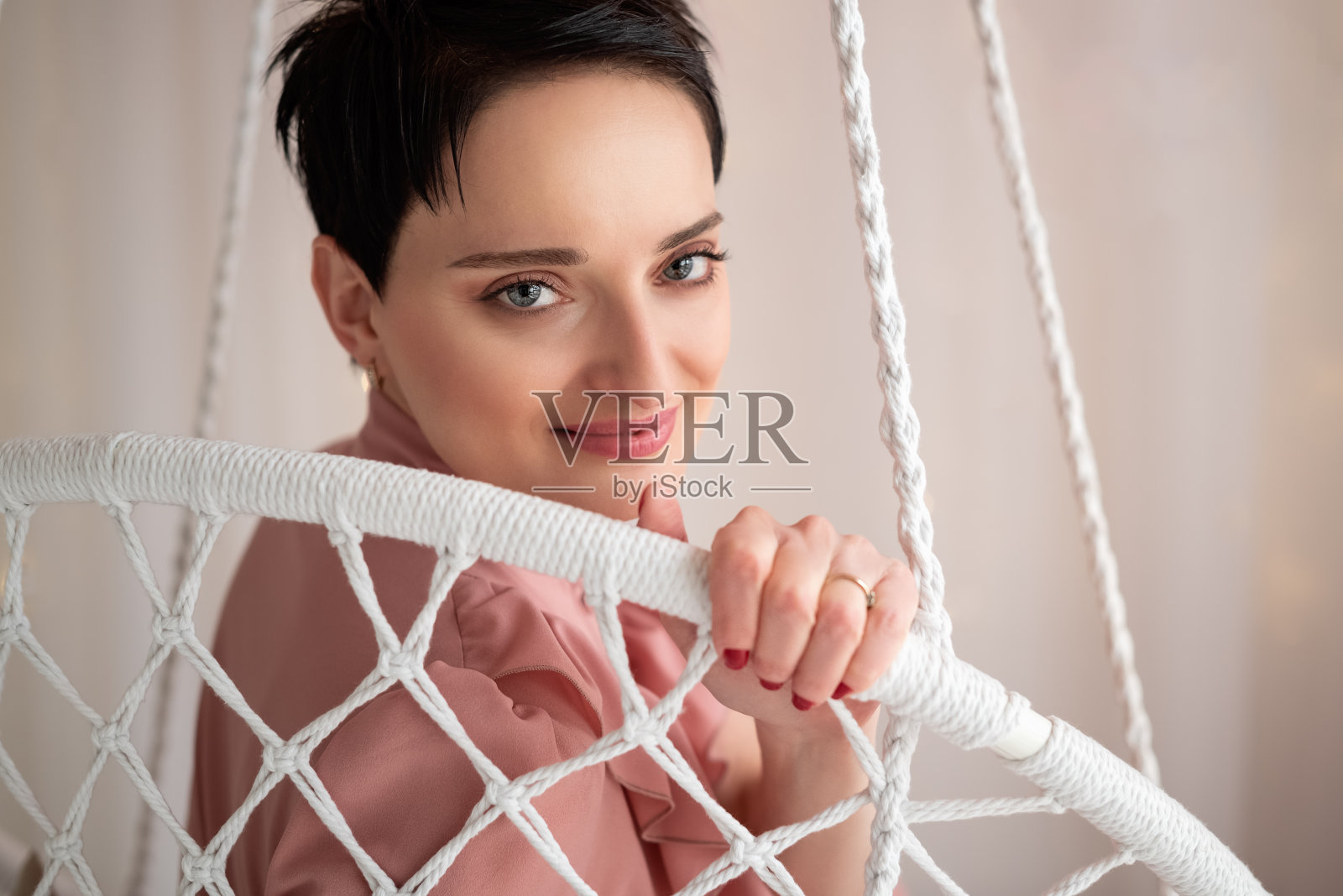 年轻迷人的黑发女孩坐在半转的柳条秋千上照片摄影图片