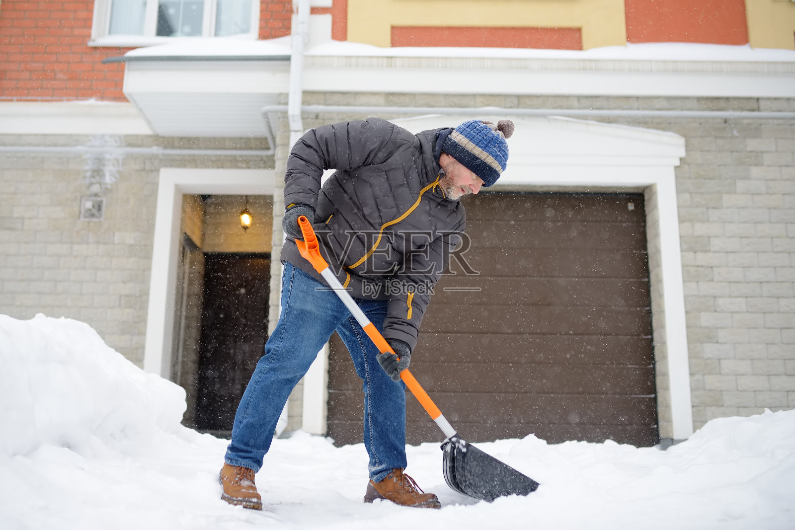 一名成熟的男子在暴风雪中清理房子附近的积雪。有人在铲车道上的雪。巨大的雪堆中。一场暴风雪过后，这个城市的困难处境照片摄影图片